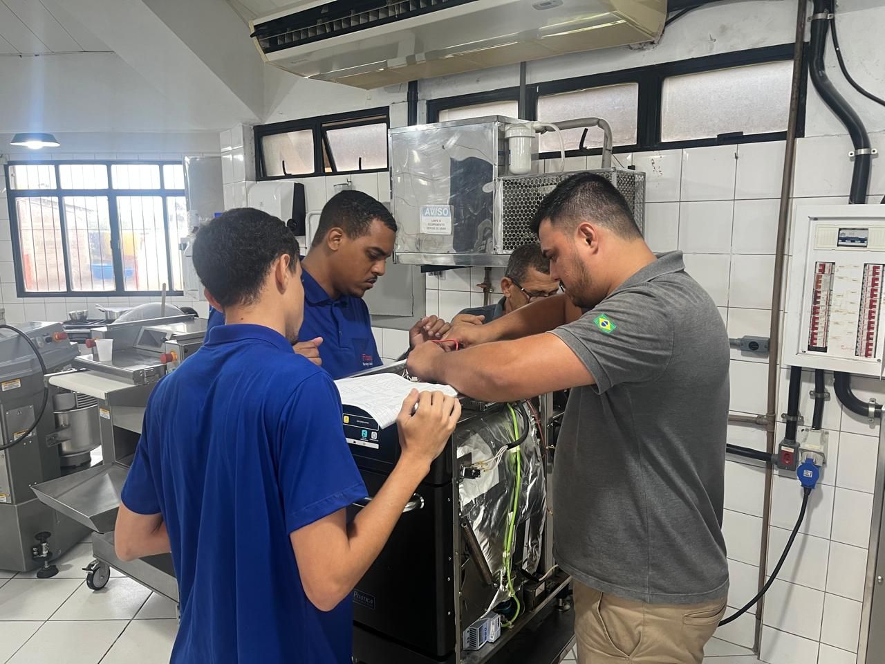 Quatro pessoas trabalhando em máquinas em um ambiente industrial bem iluminado.