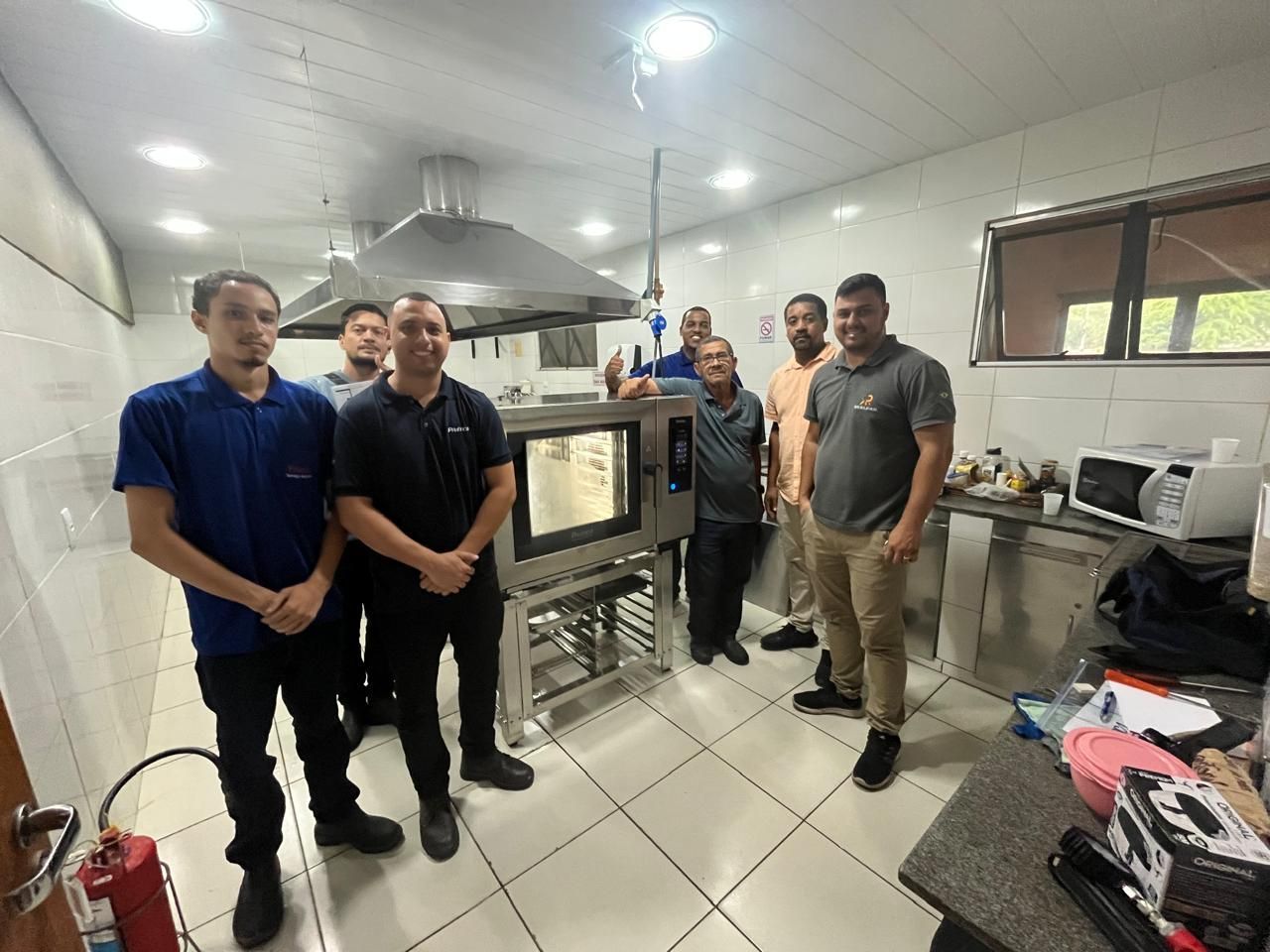 Um grupo de pessoas está em uma cozinha industrial com um forno.