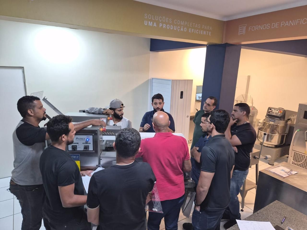 Grupo de homens reunidos em torno de uma máquina de panificação