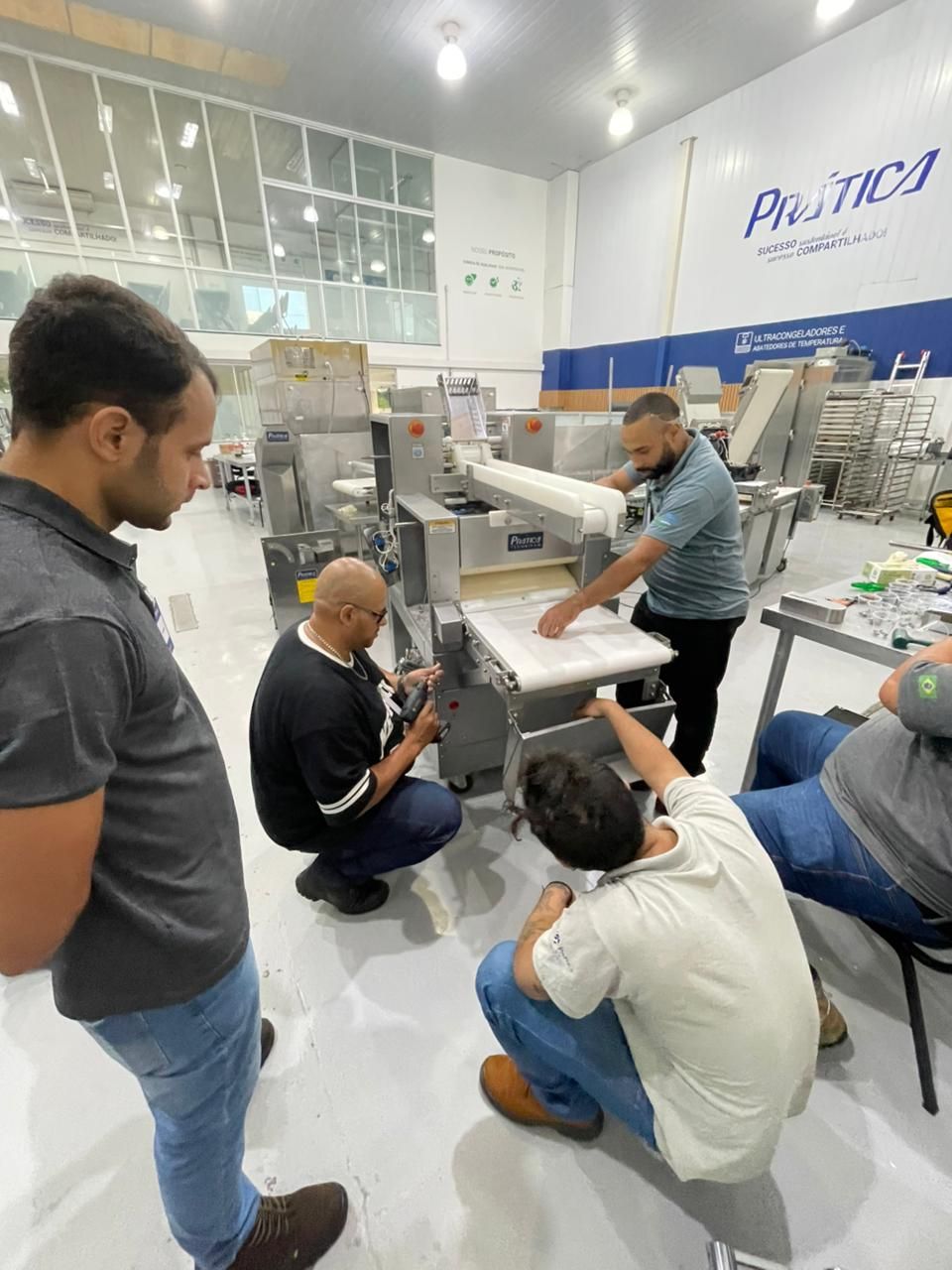 Homens trabalhando em máquinas em uma oficina. Um homem alimenta a máquina com papel. Outros observam e trabalham.