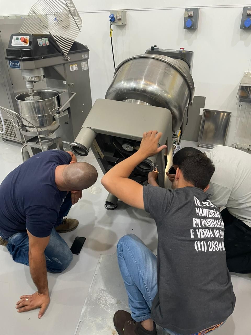 Três homens trabalhando em uma grande batedeira industrial em uma cozinha.