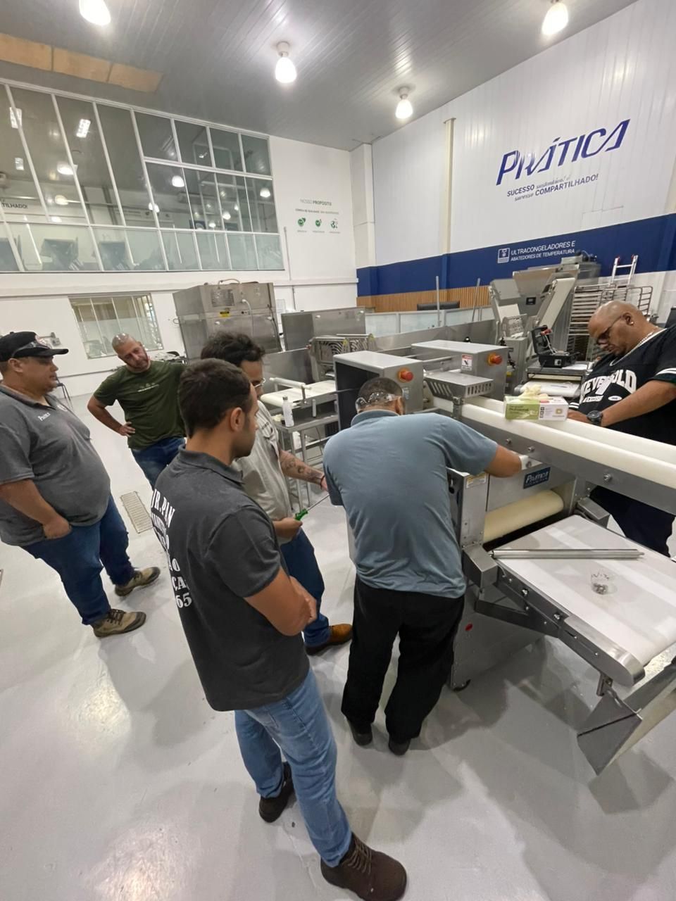 Grupo de homens observando máquinas em uma fábrica de processamento de alimentos; um deles está operando um dos equipamentos