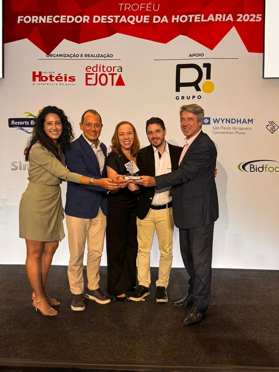 Cinco pessoas segurando um prêmio em um palco; elas estão sorrindo.