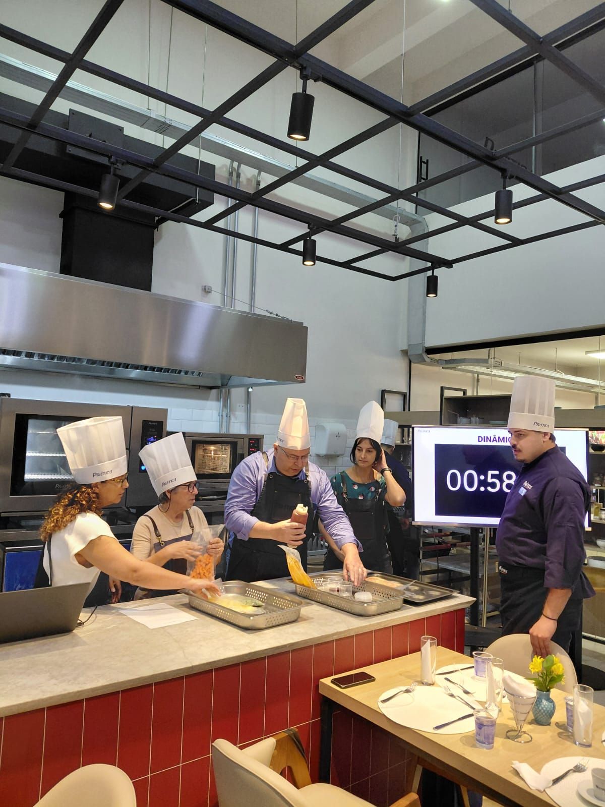 Chefs de chapéu branco cozinhando em uma bancada com um cronômetro em uma tela.