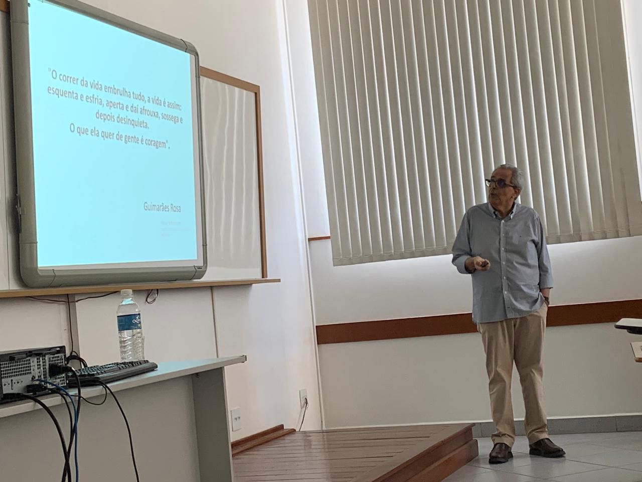 Um homem está em pé em frente a uma tela de projetor em uma sala de aula.
