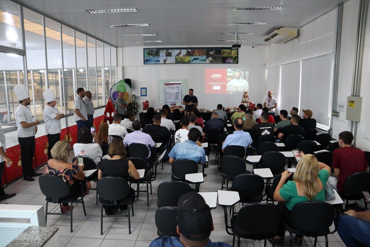 Um grande grupo de pessoas está sentado em uma sala assistindo a uma apresentação