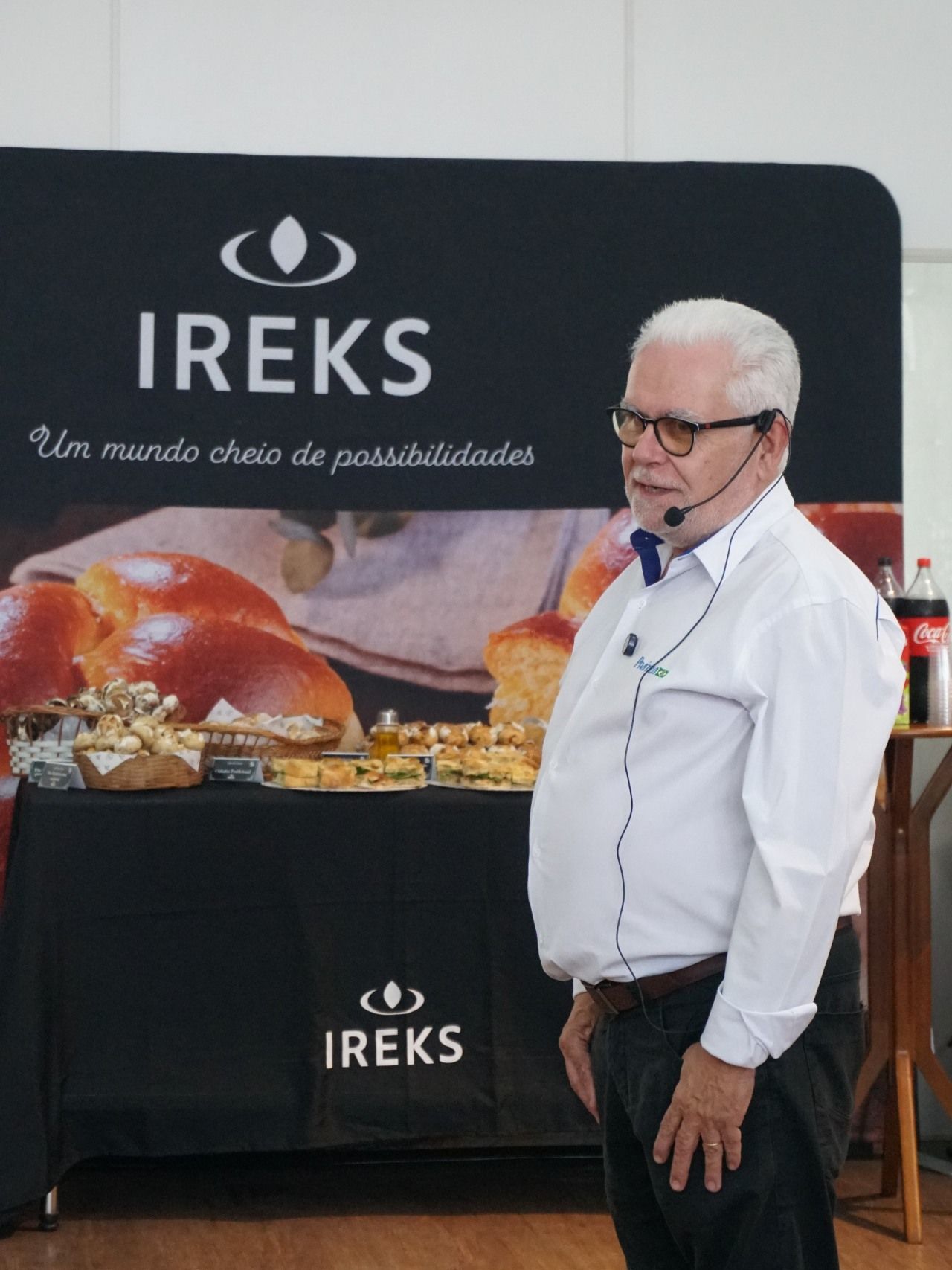 Homem de camisa branca e óculos discursa em evento do IREKS.