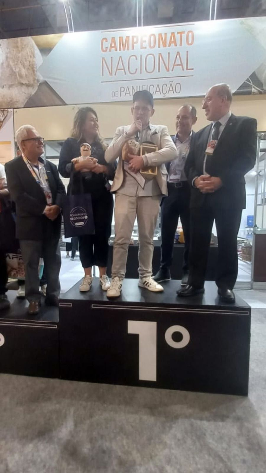 Um grupo de pessoas está em um pódio segurando troféus.