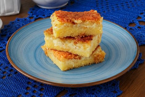 Bolo de fubá cremoso com queijo em um prato azul, sobre uma toalha de mesa azul de crochê.