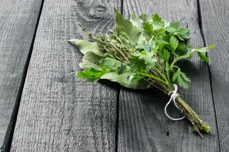 Feixe de ervas frescas amarradas com barbante em uma superfície de madeira desgastada.