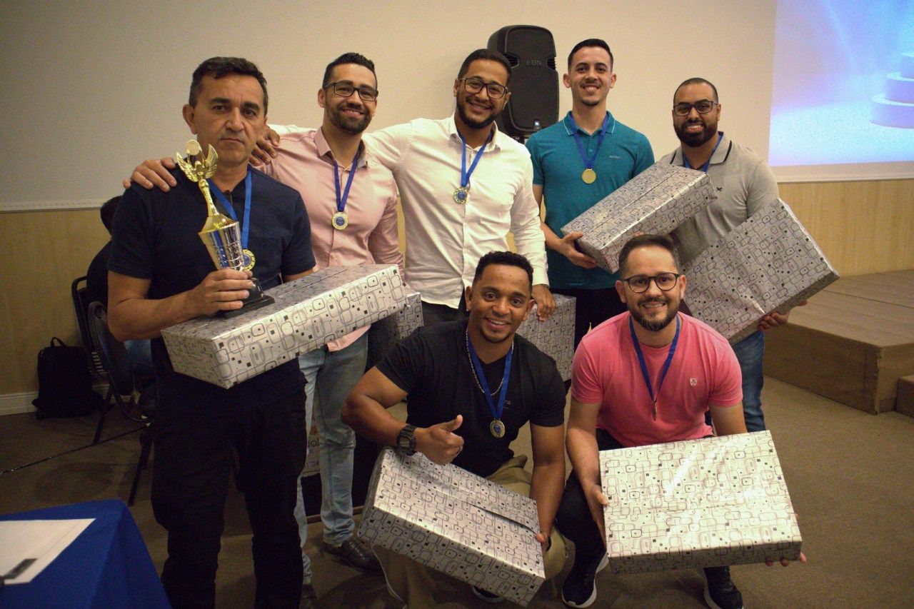 Um grupo de homens está posando para uma foto enquanto segura presentes e troféus.
