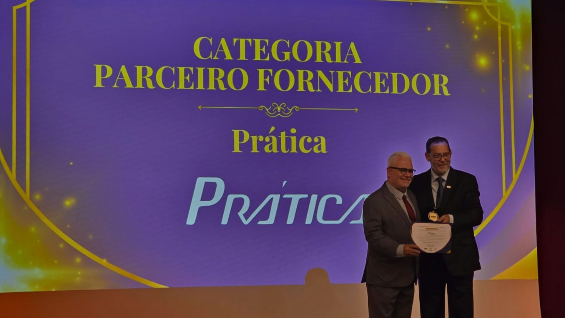 Dois homens em pé em frente a uma tela que diz