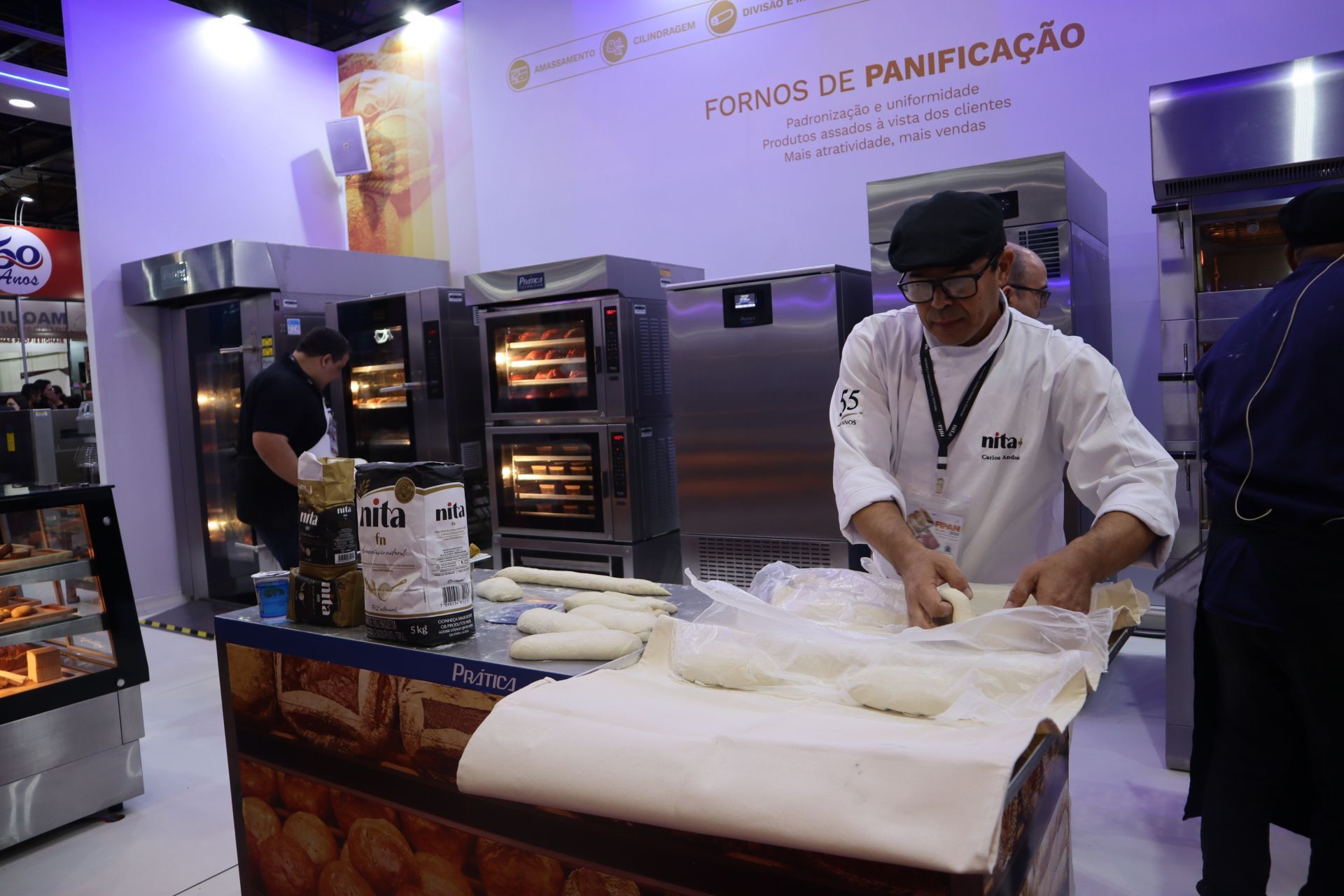 A man is kneading dough in front of a sign that says fornos de panificação