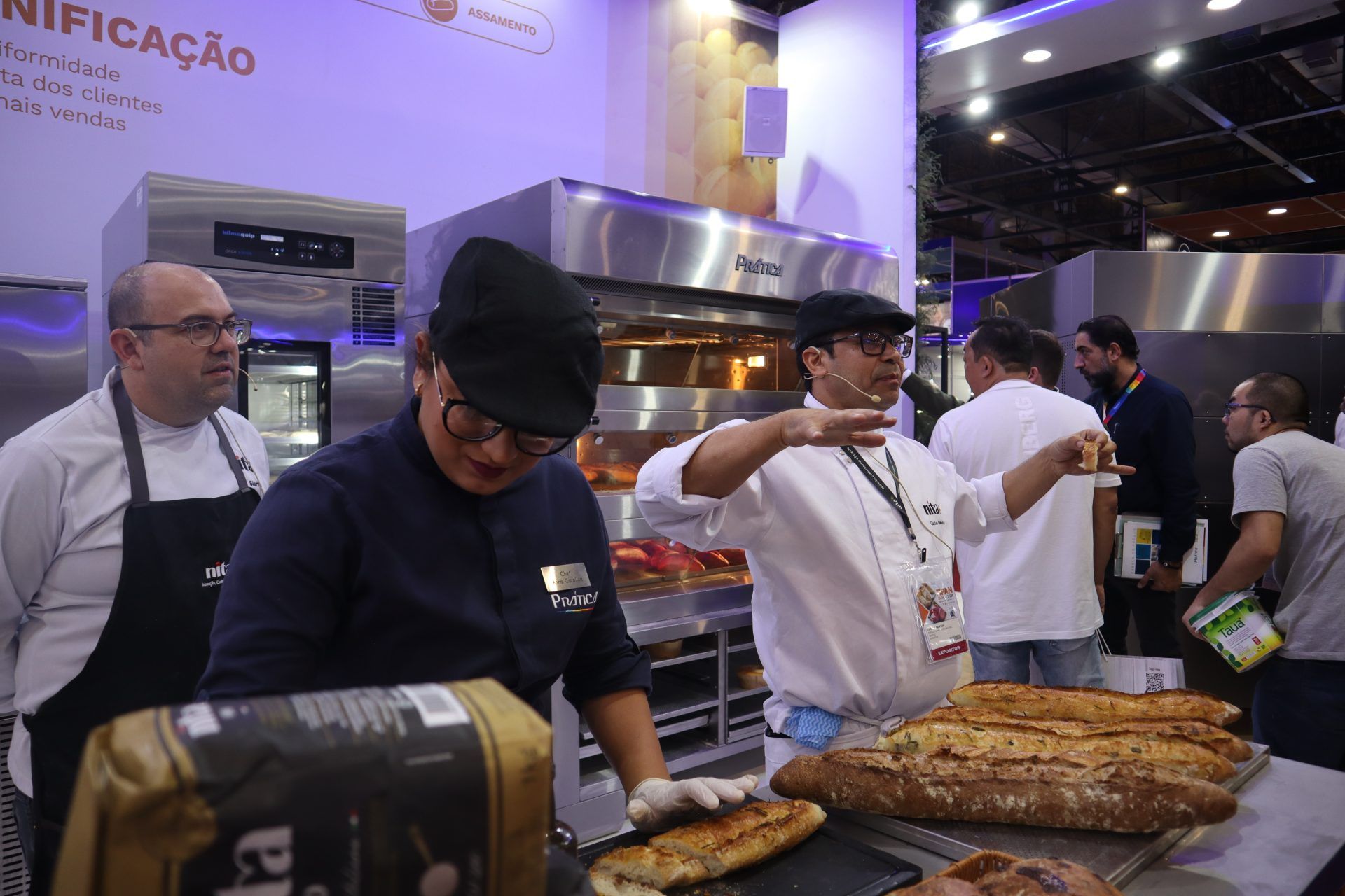 Um grupo de pessoas está de pé ao redor de uma mesa com pão sobre ela.