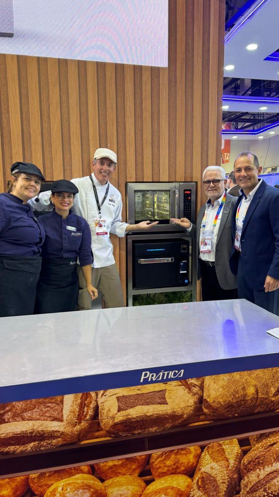Um grupo de pessoas está em pé ao redor de uma mesa em frente a uma padaria.