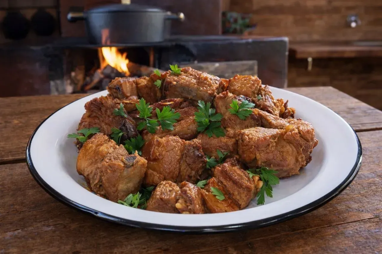 Carne de lata mineira servida em prato esmaltado, com cubos de carne de porco dourados na banha