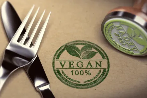 Faca, garfo e carimbo vegano em superfície marrom texturizada.