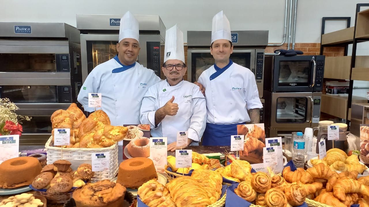 Três chefs posam para uma foto em frente a uma mesa cheia de comida.