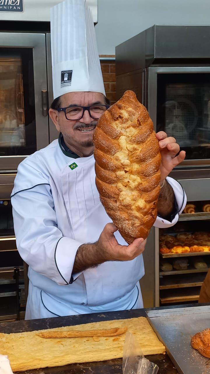 Um homem com chapéu de chef está segurando um pedaço de pão
