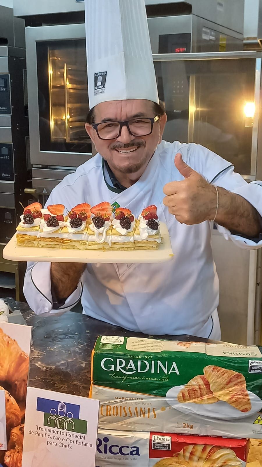 Um chef está segurando uma bandeja de comida e fazendo sinal de positivo.