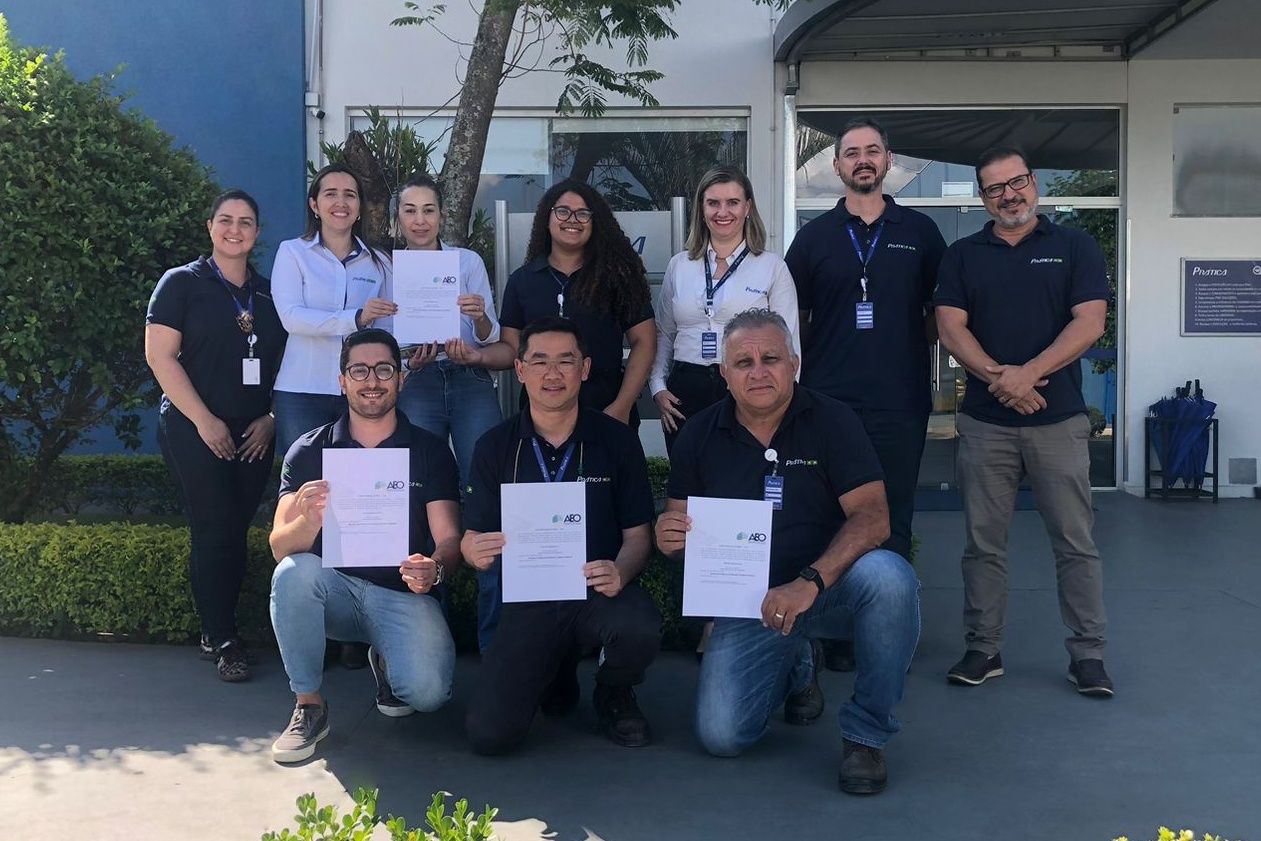 Grupo de pessoas, dentro e fora do prédio, segurando papéis e sorrindo. A fachada do edifício aparece ao fundo.