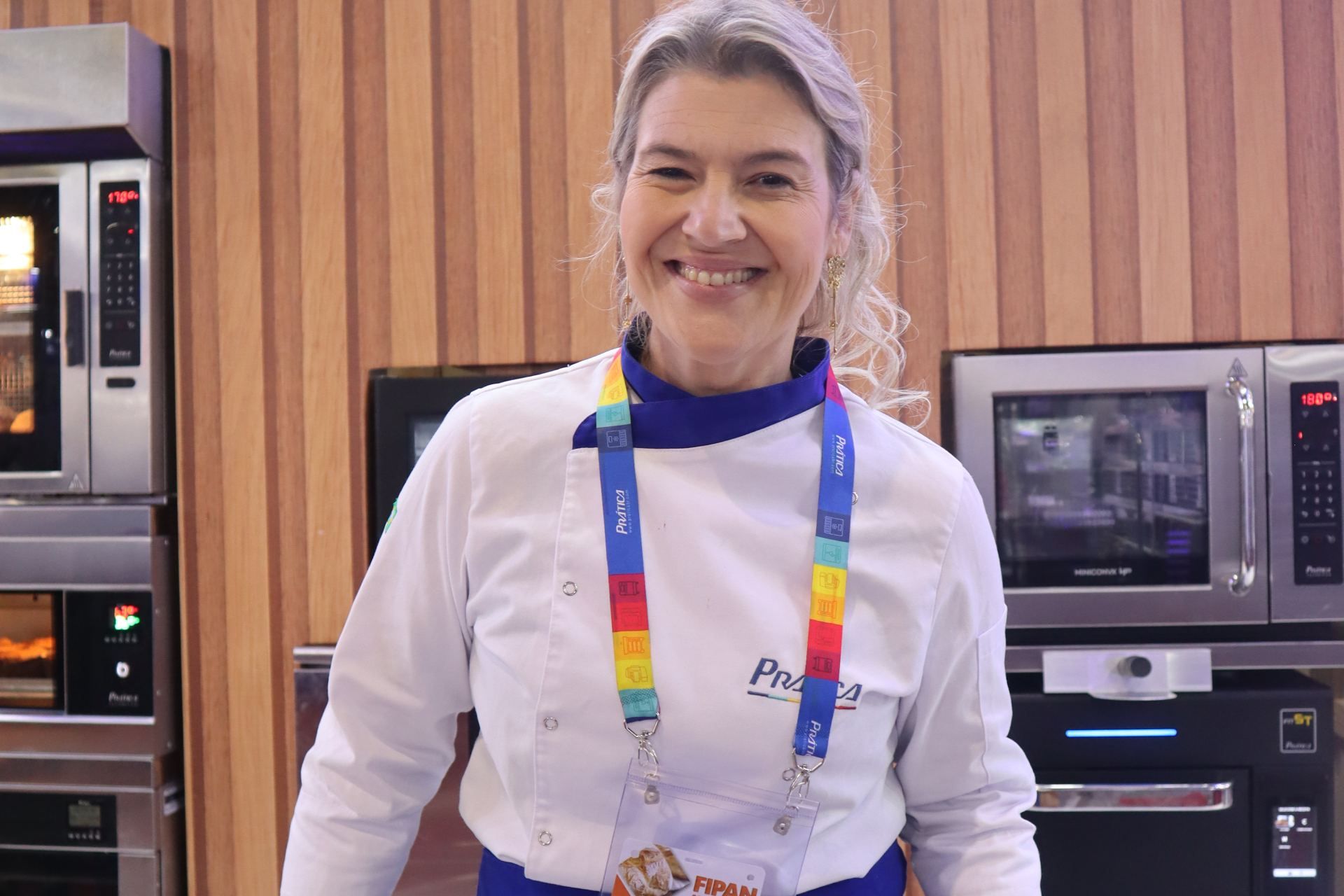 Uma mulher em uniforme de chef sorri em frente a vários fornos.