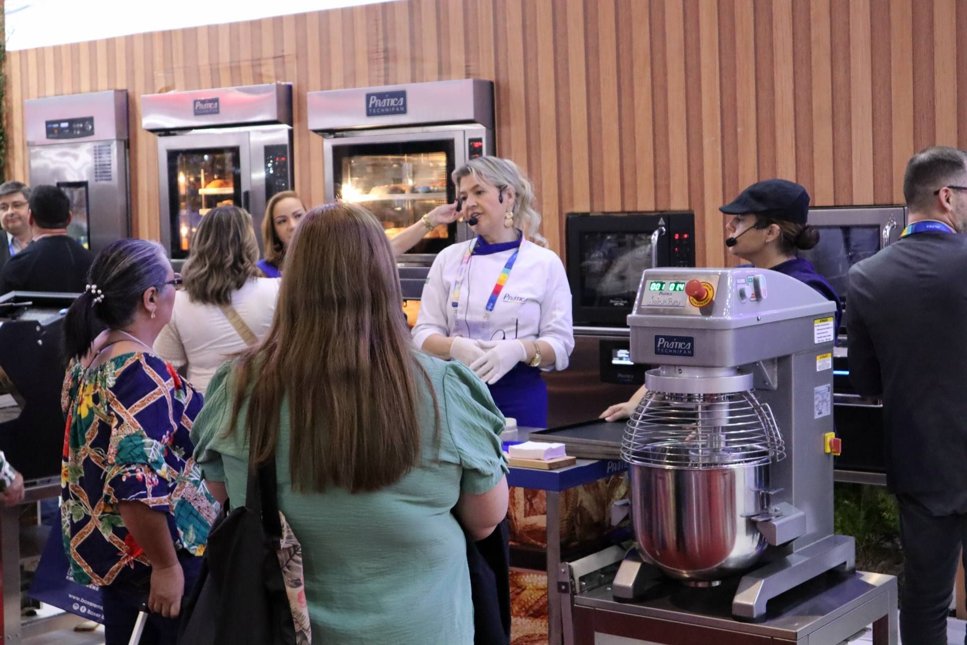Um grupo de pessoas está em volta de uma batedeira em uma padaria.