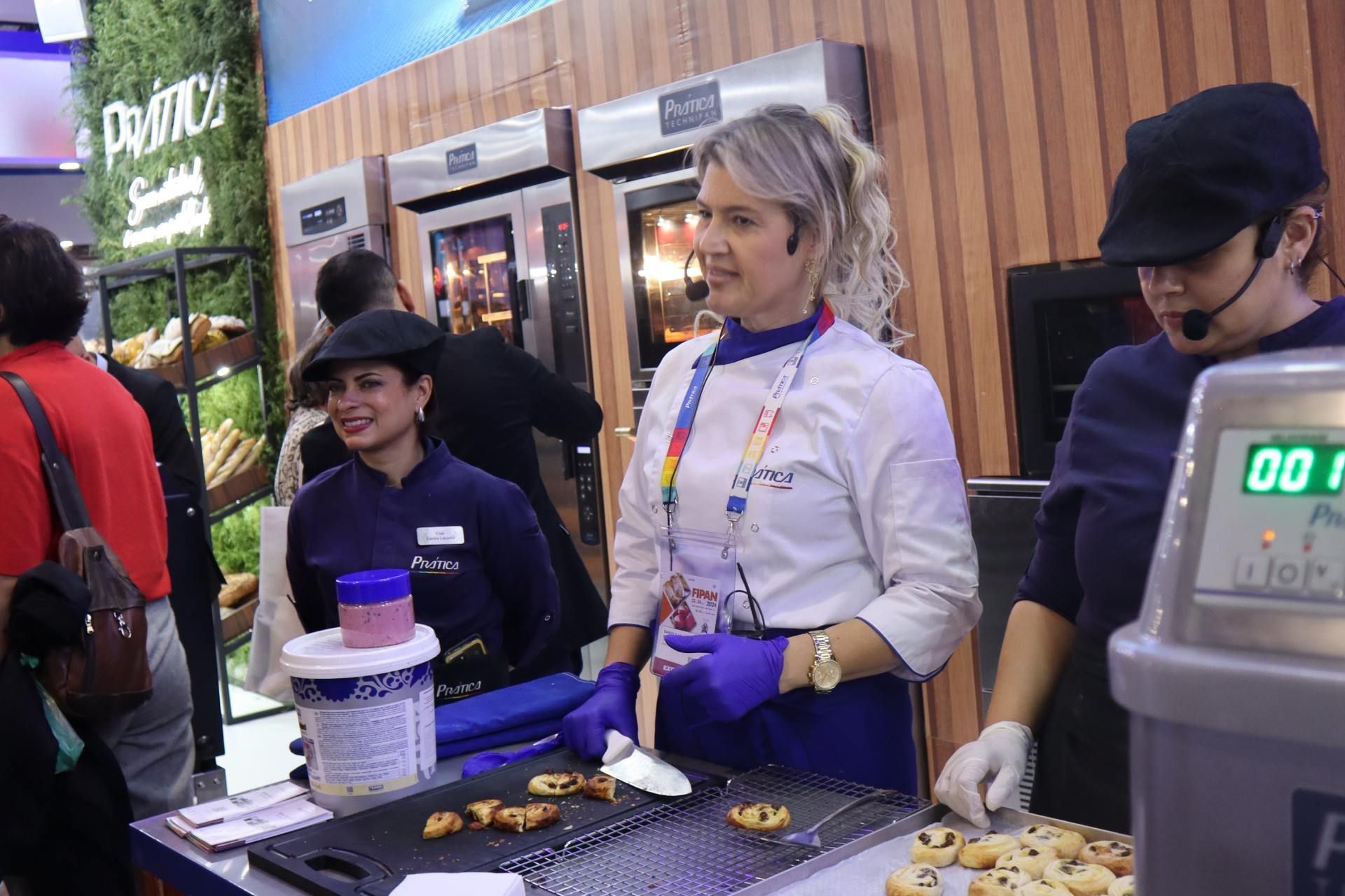 Um grupo de pessoas está em pé ao redor de uma mesa em uma padaria.