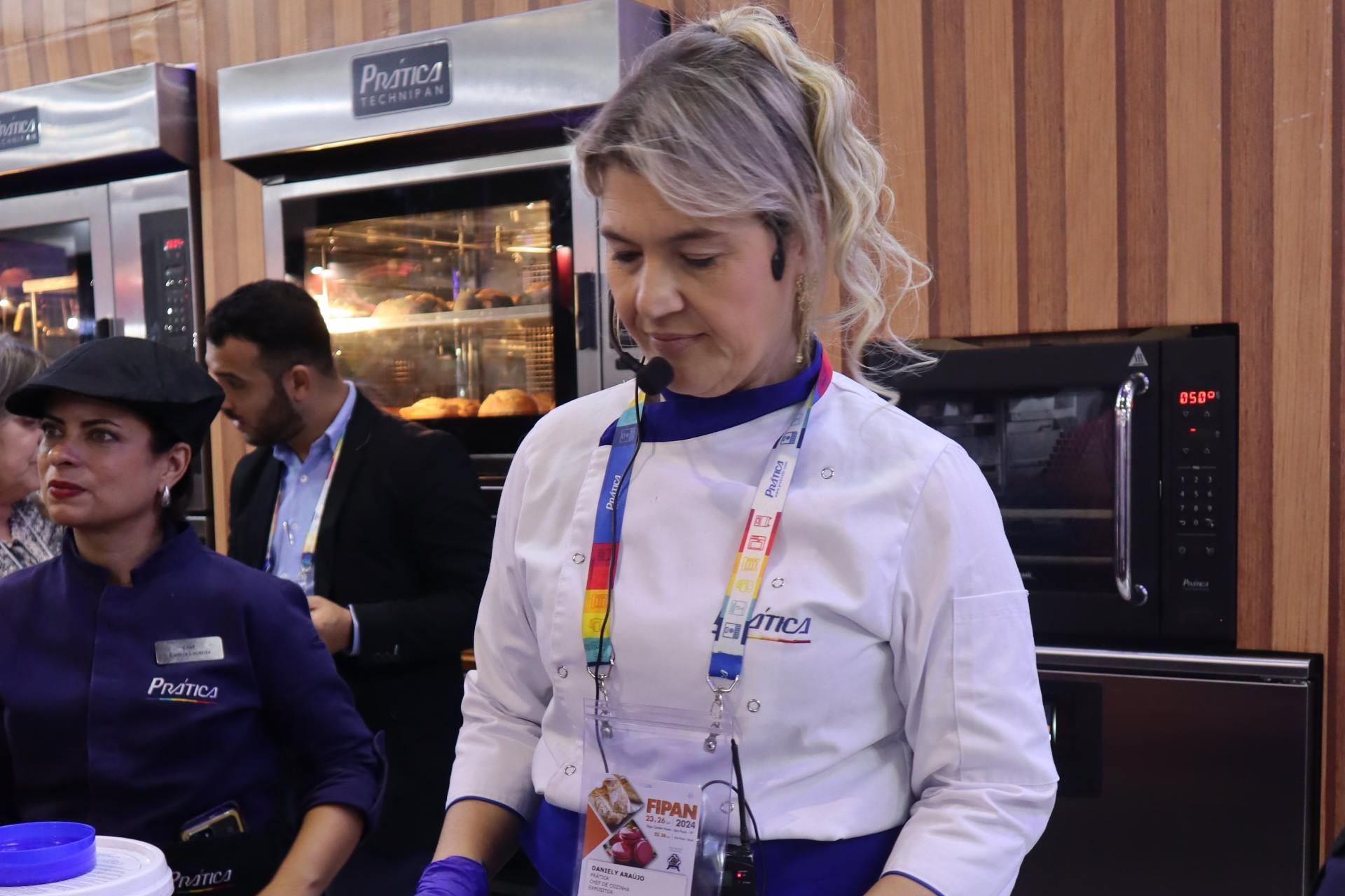 Uma mulher em uniforme de chef está parada em frente a um forno.