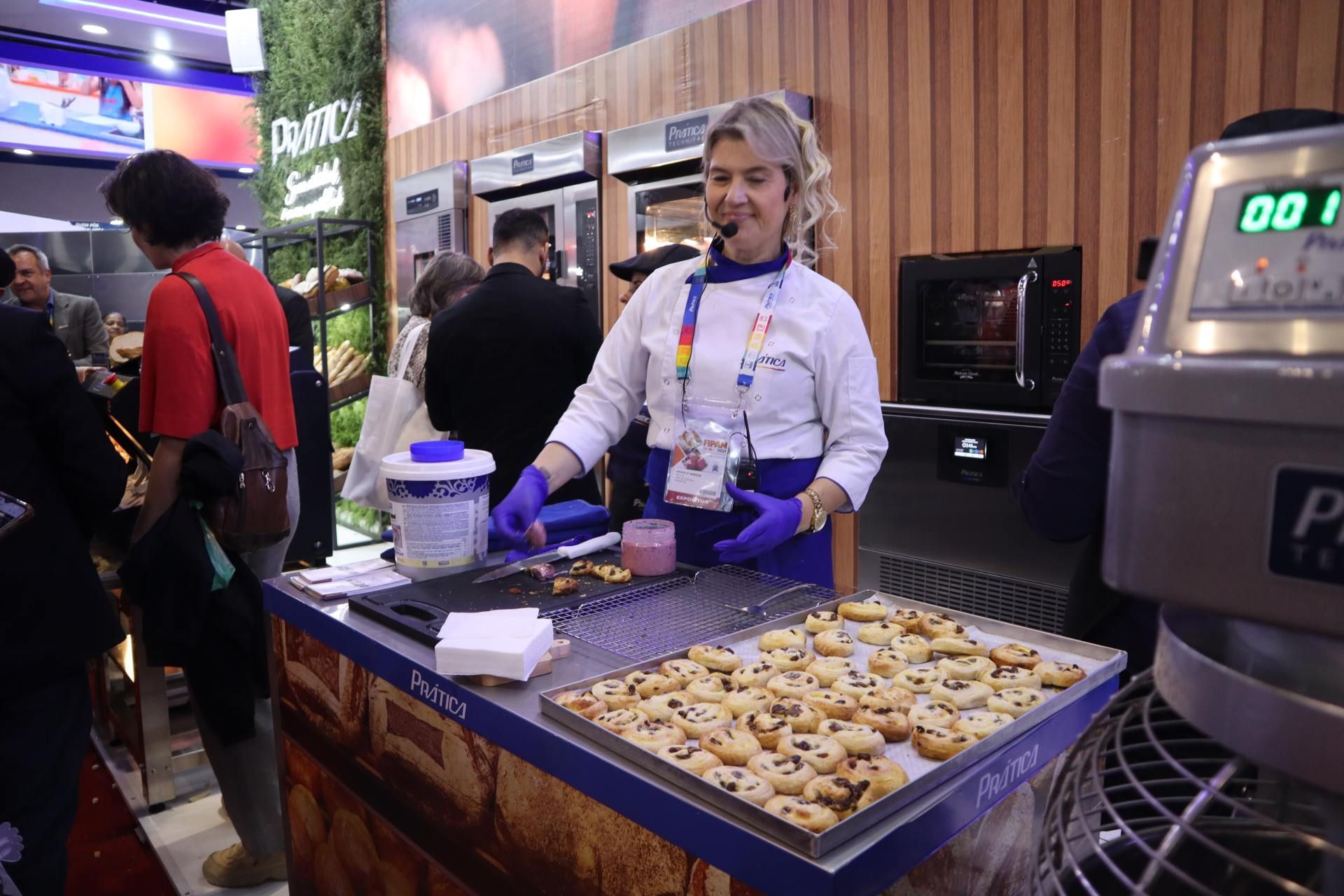 Uma mulher está de pé atrás de uma mesa com uma bandeja de biscoitos sobre ela.