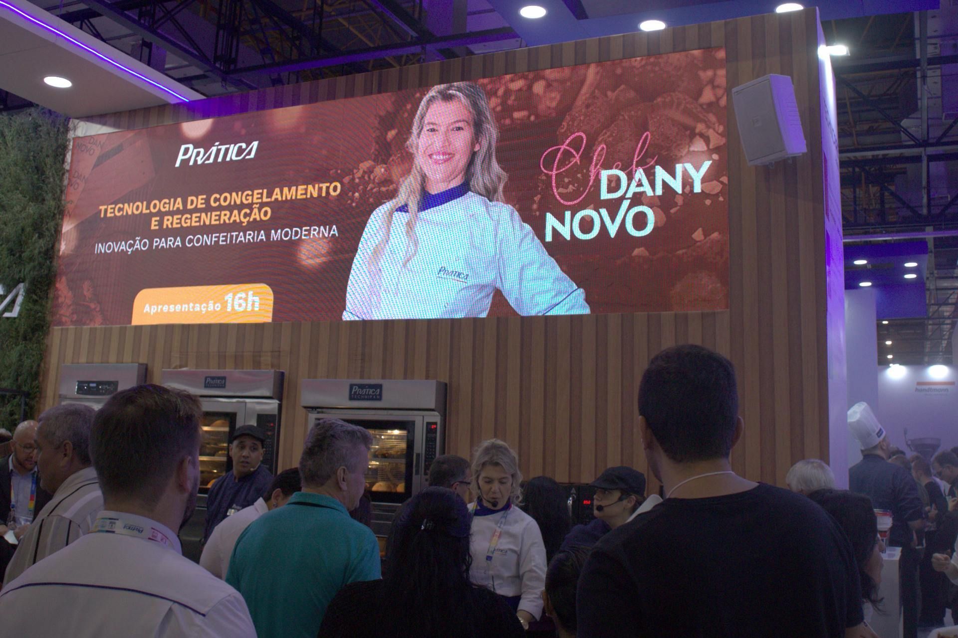 Um grupo de pessoas está em frente a uma tela grande que diz dany novo.