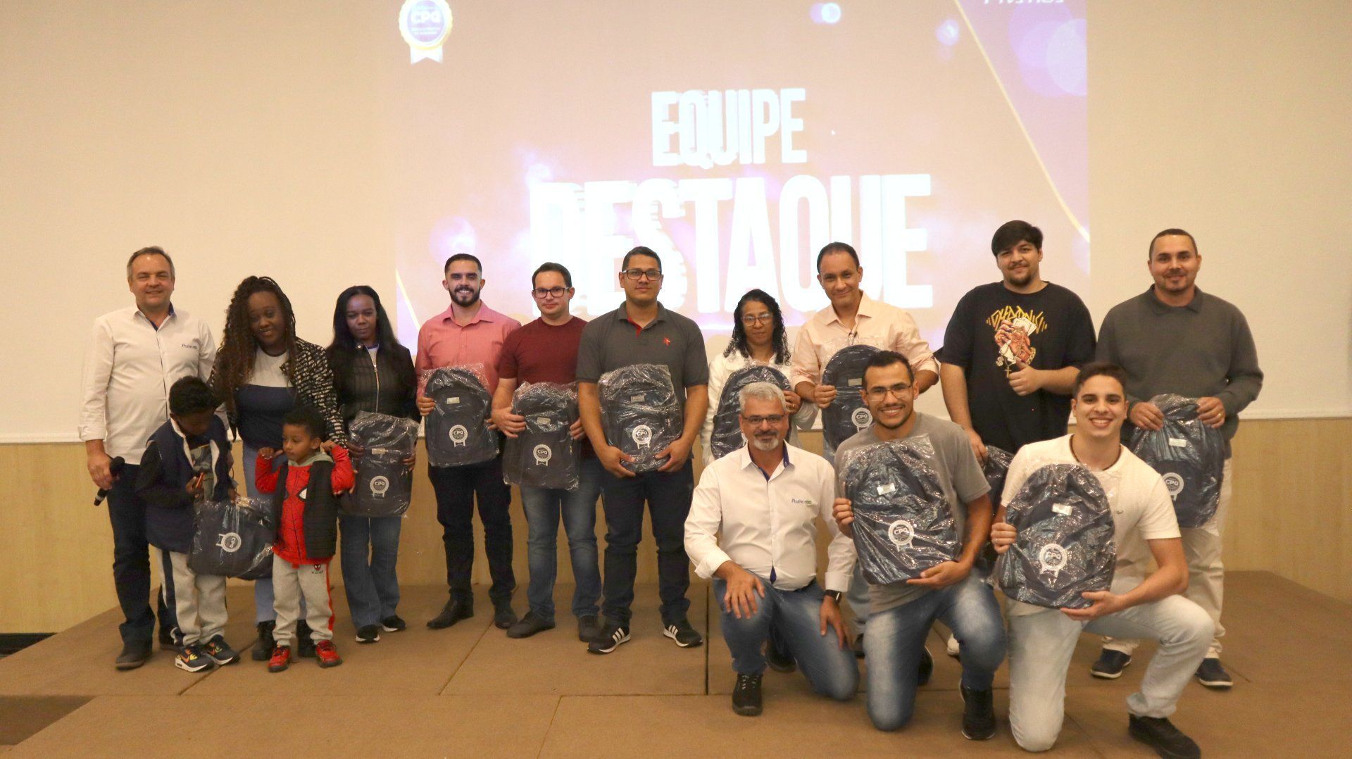 Um grupo de pessoas está posando para uma foto em frente a uma tela grande.