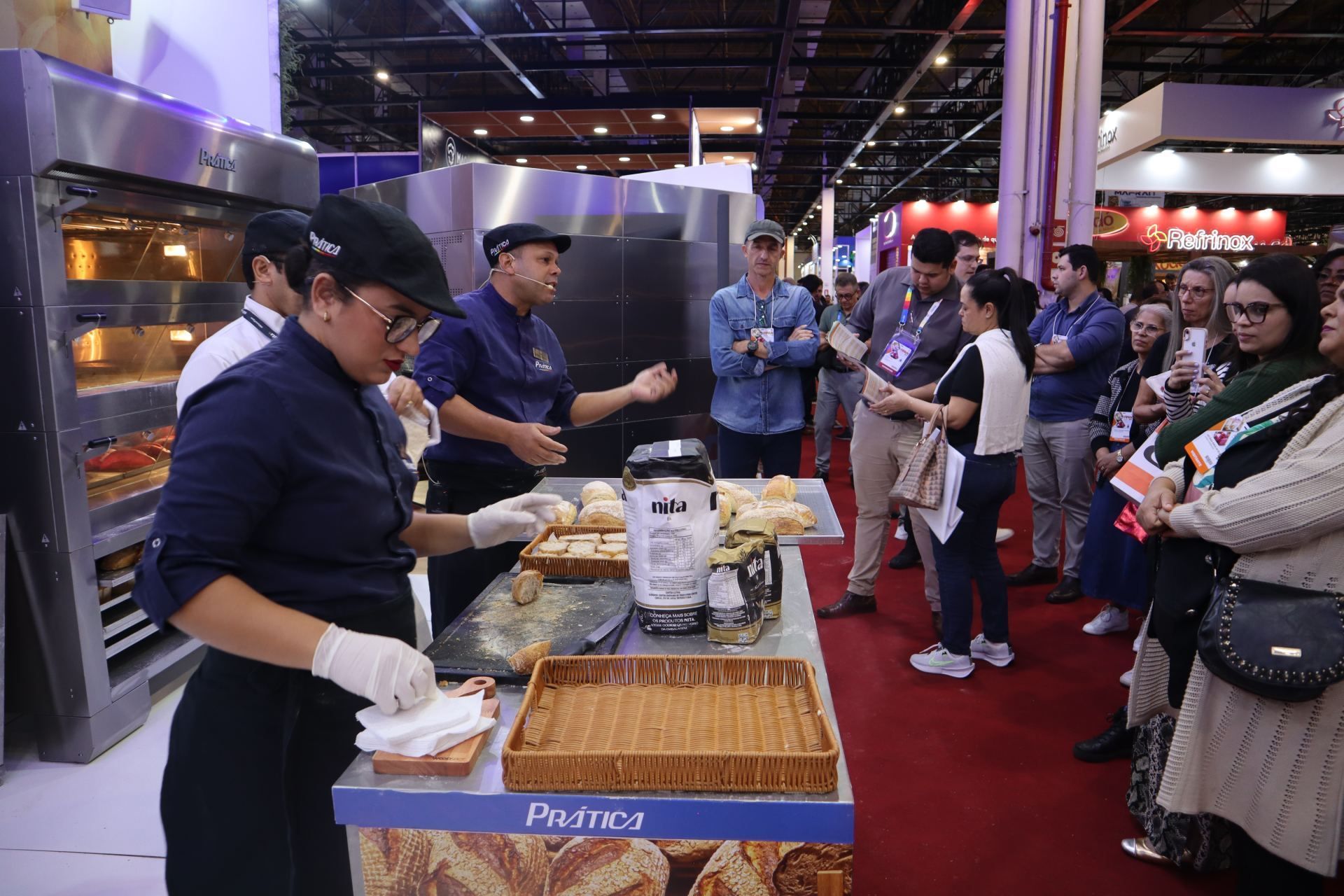 Um grupo de pessoas está em pé ao redor de uma mesa em uma padaria.