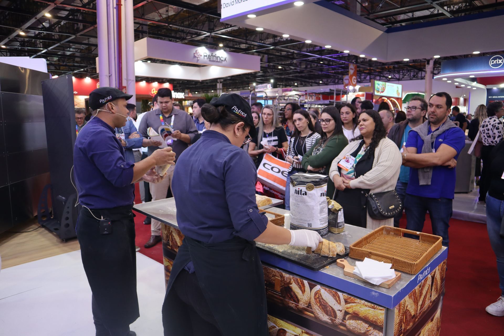 Um grupo de pessoas está em volta de uma barraca de comida em uma convenção.