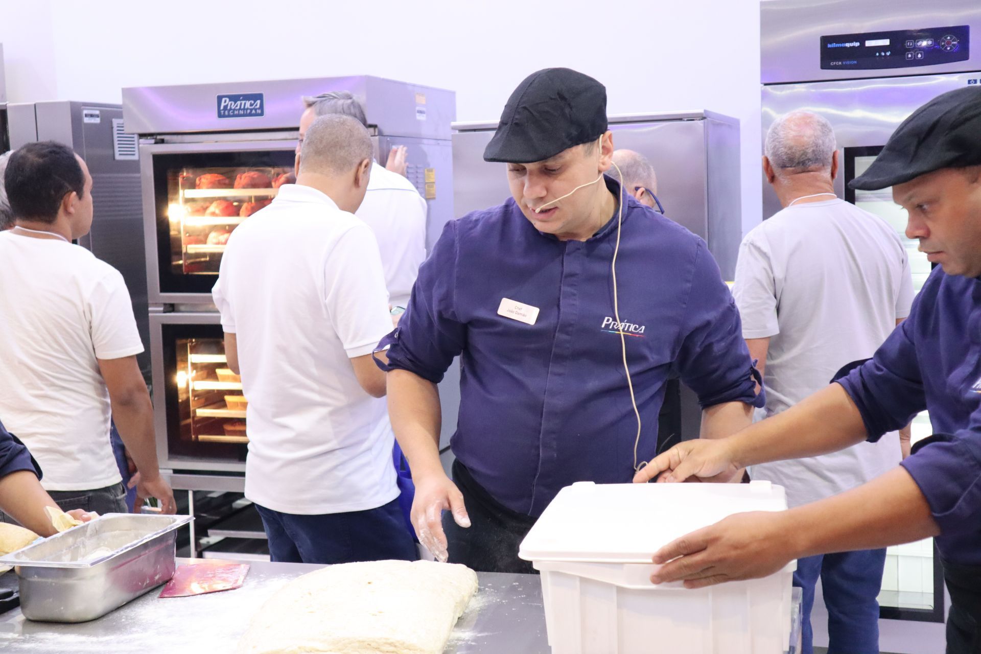 Um grupo de homens está em pé ao redor de uma mesa na cozinha.