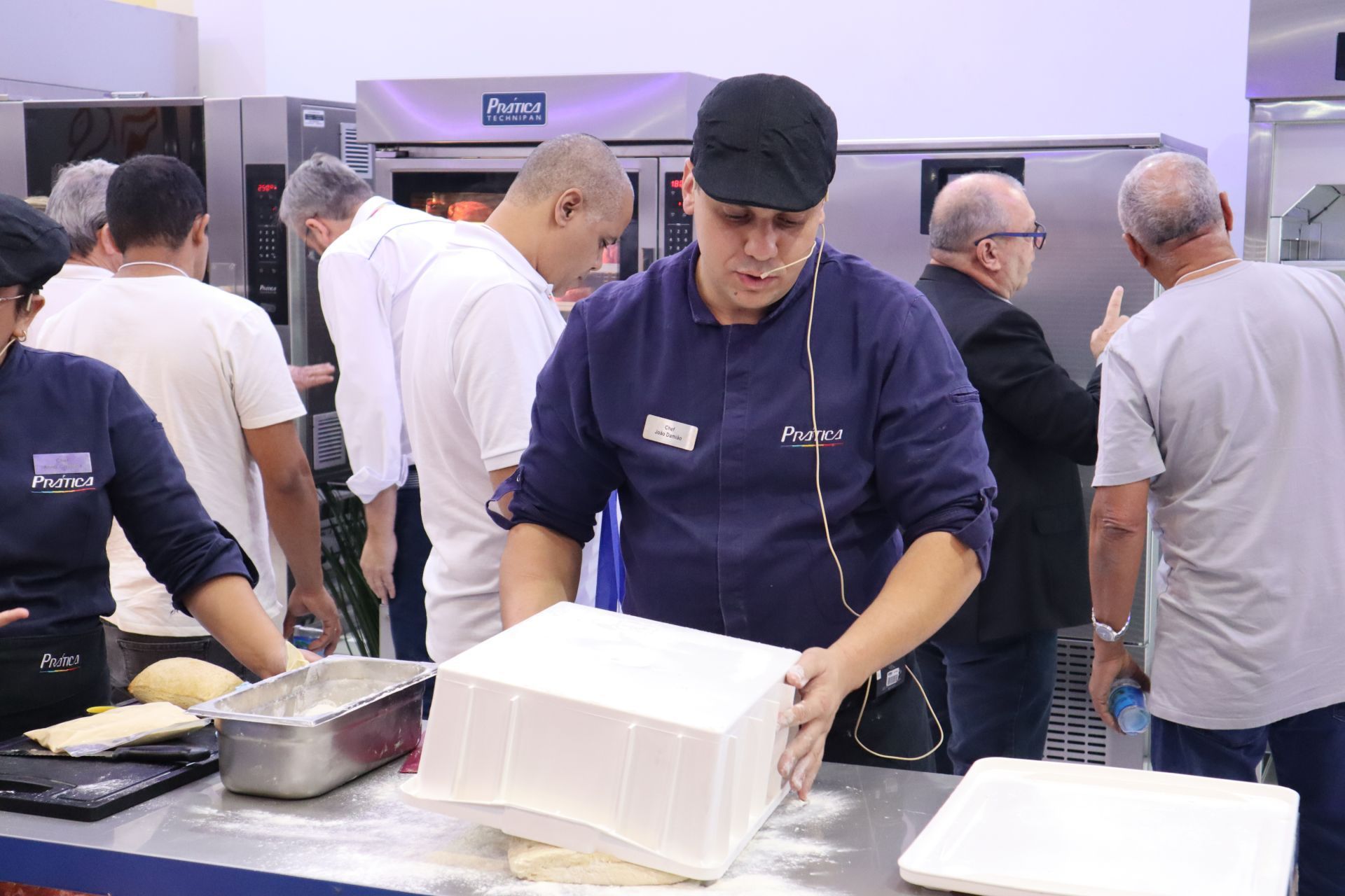 Um grupo de pessoas está em pé ao redor de uma mesa na cozinha.