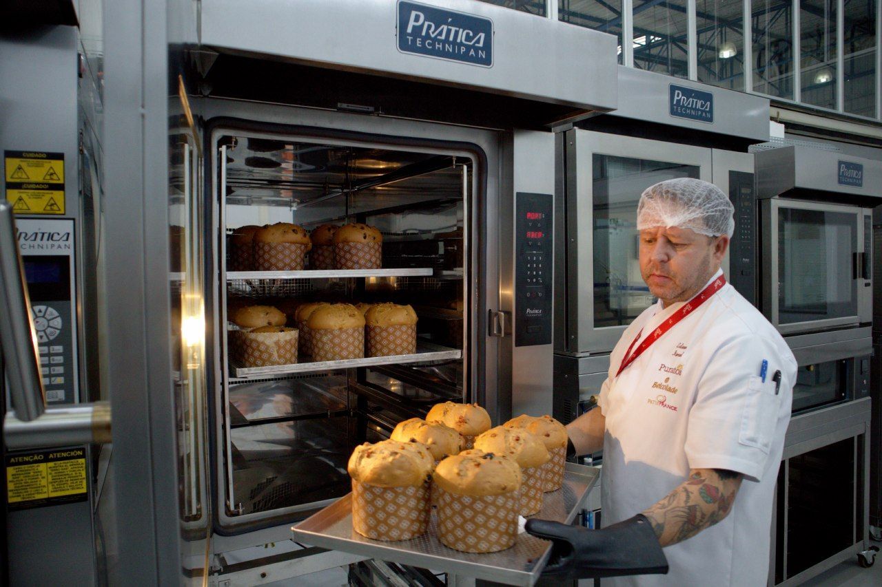 Um homem está segurando uma bandeja de pão em frente a um forno.