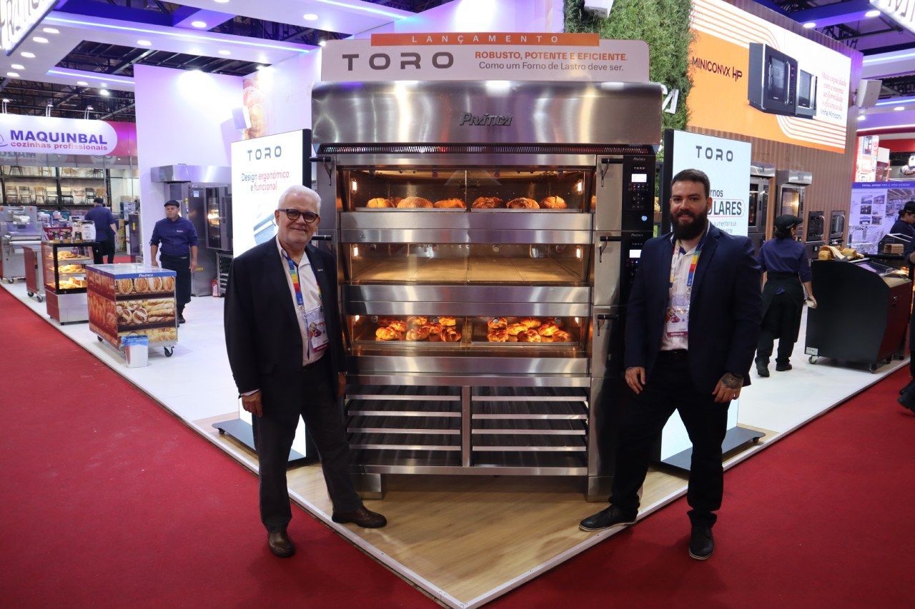 Dois homens estão em frente a um grande forno em uma padaria.