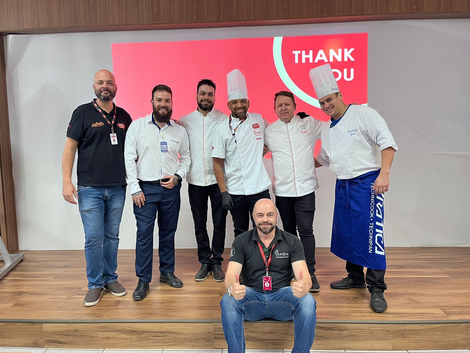 Um grupo de homens está posando para uma foto em frente a uma placa de agradecimento.