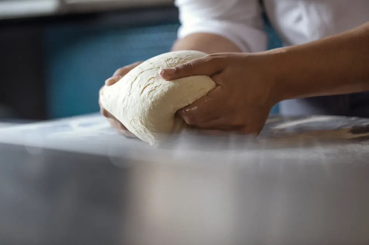 Uma pessoa está amassando massa sobre uma mesa.