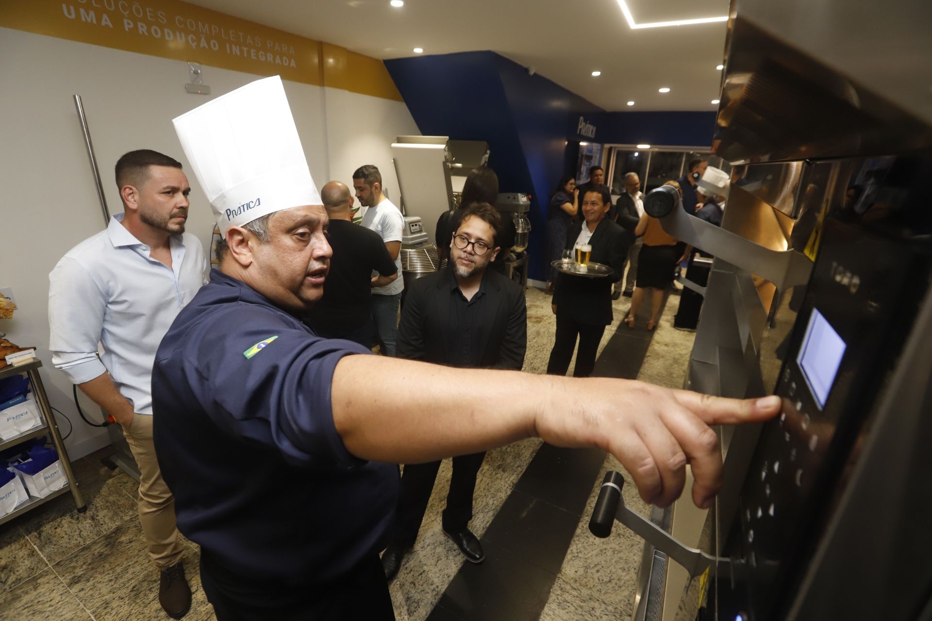 O chef aponta para o painel de controle de um forno na cozinha, demonstrando aos espectadores.