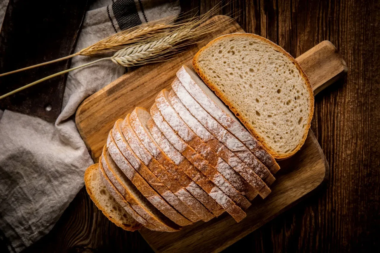 Fatias de pão sobre tábua de madeira com talos de trigo e um pano de linho.