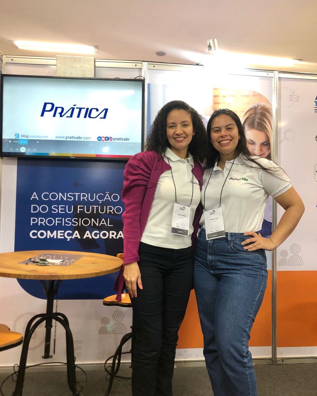 Duas mulheres posam para uma foto em frente a uma placa que diz prática