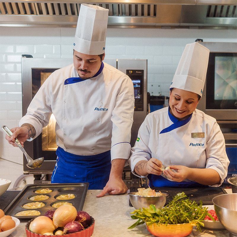Dois chefs de jaleco e chapéu brancos cozinhando em uma cozinha.