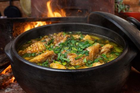 Frango caipira mineiro em panela de barro com fogão à lenha ao fundo.