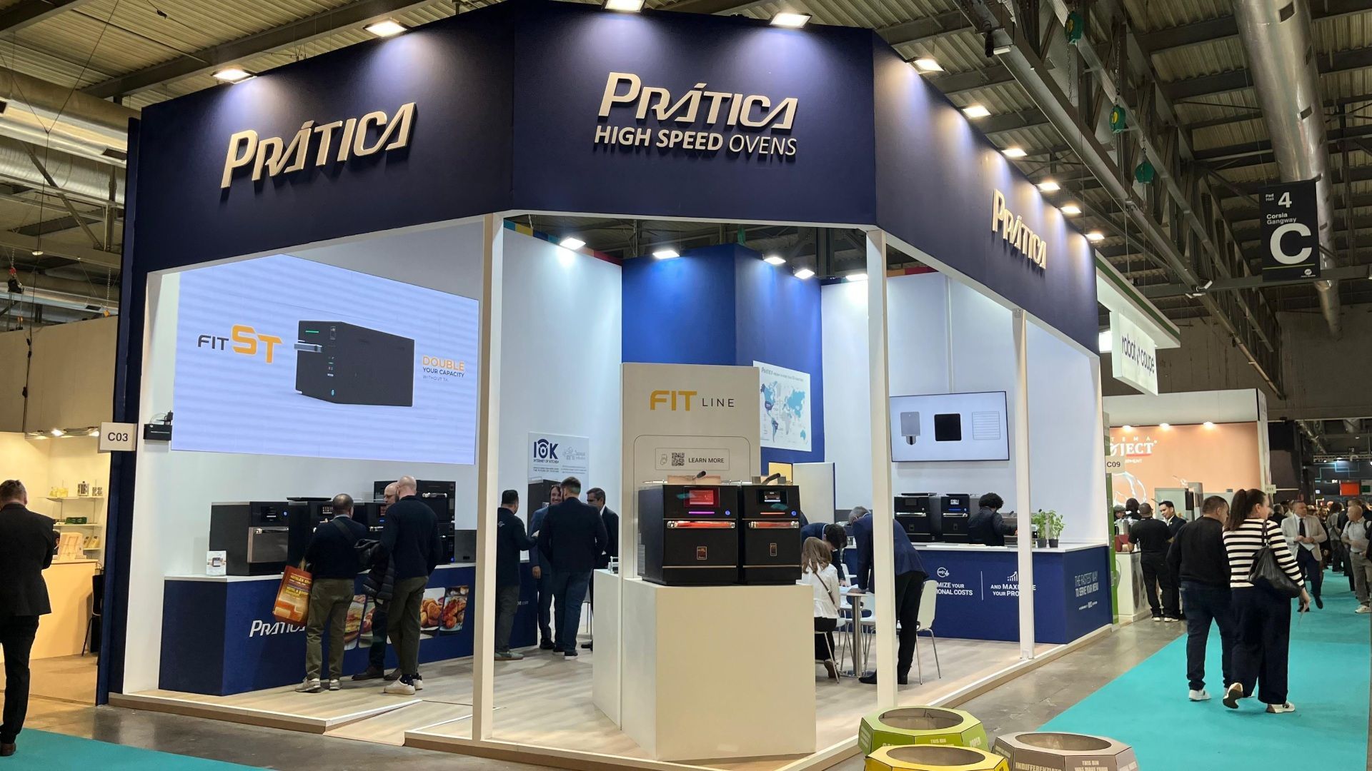 Um estande da Prática, com a marca azul e branca, produtos expostos e pessoas olhando a loja.