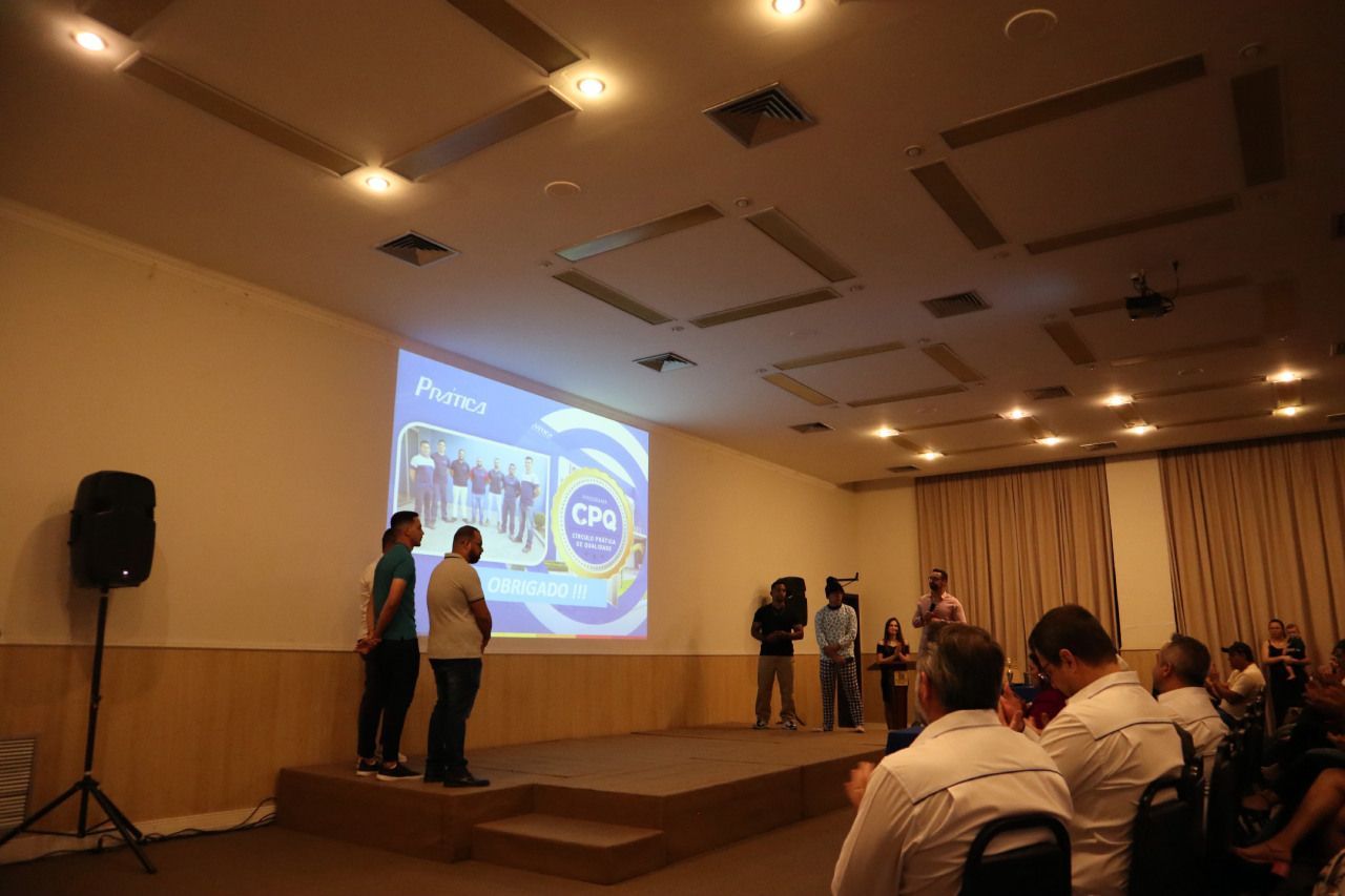 Um grupo de pessoas está em pé em um palco em frente a uma tela de projetor.