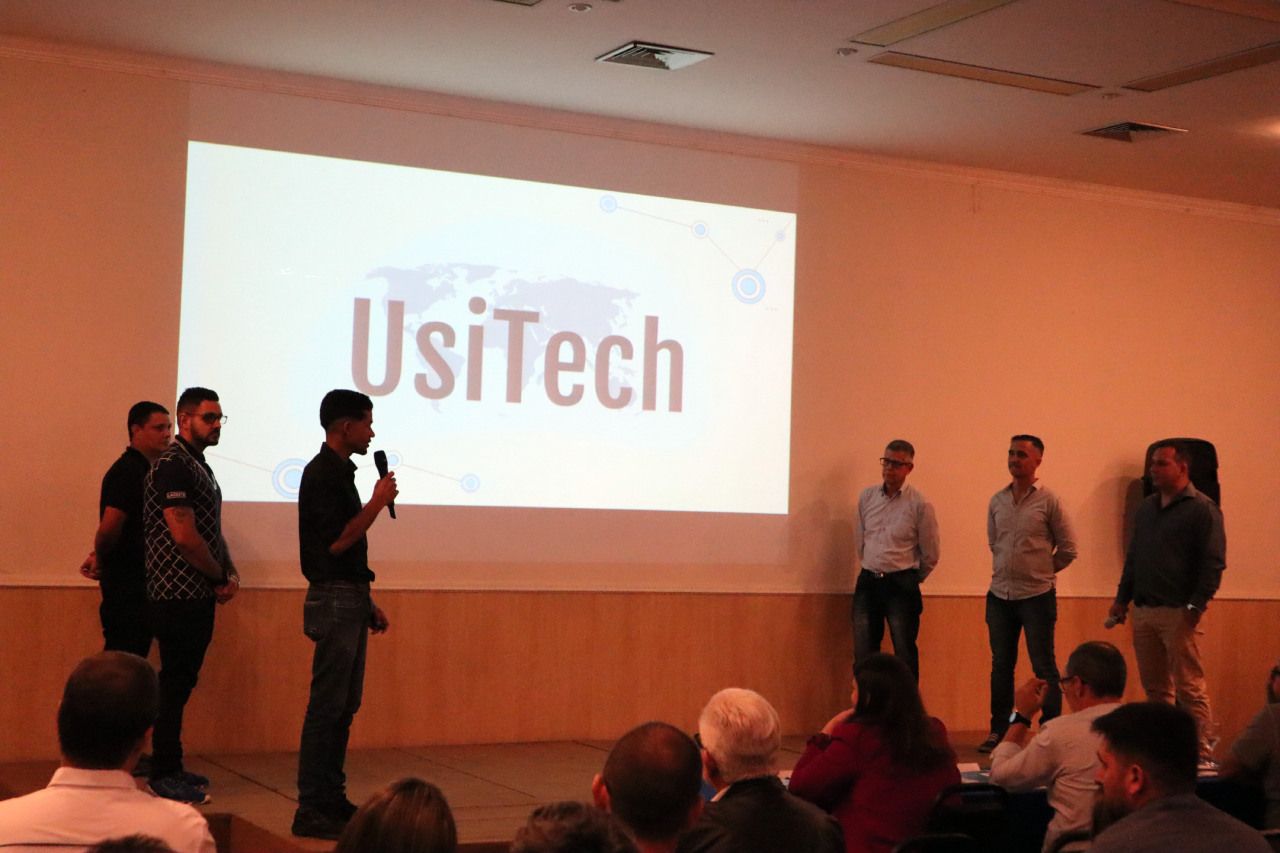 Um grupo de pessoas em pé na frente de uma tela que diz usitech
