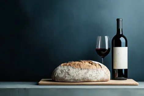Homem com barba sentado à mesa, cortando um sanduíche com uma faca; visto através de uma janela.
