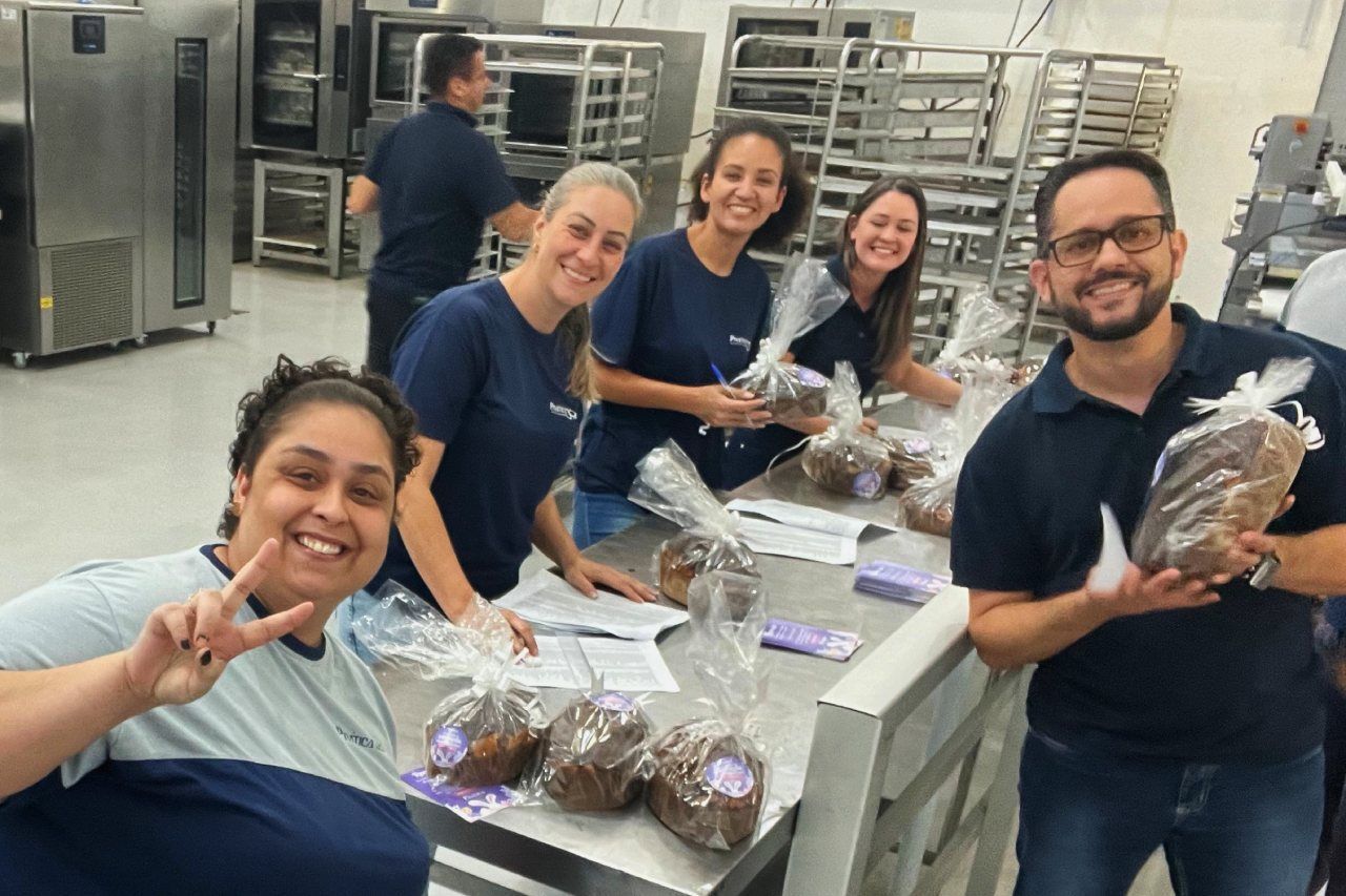 Um grupo de pessoas está em pé ao redor de uma mesa segurando sacos de pão.